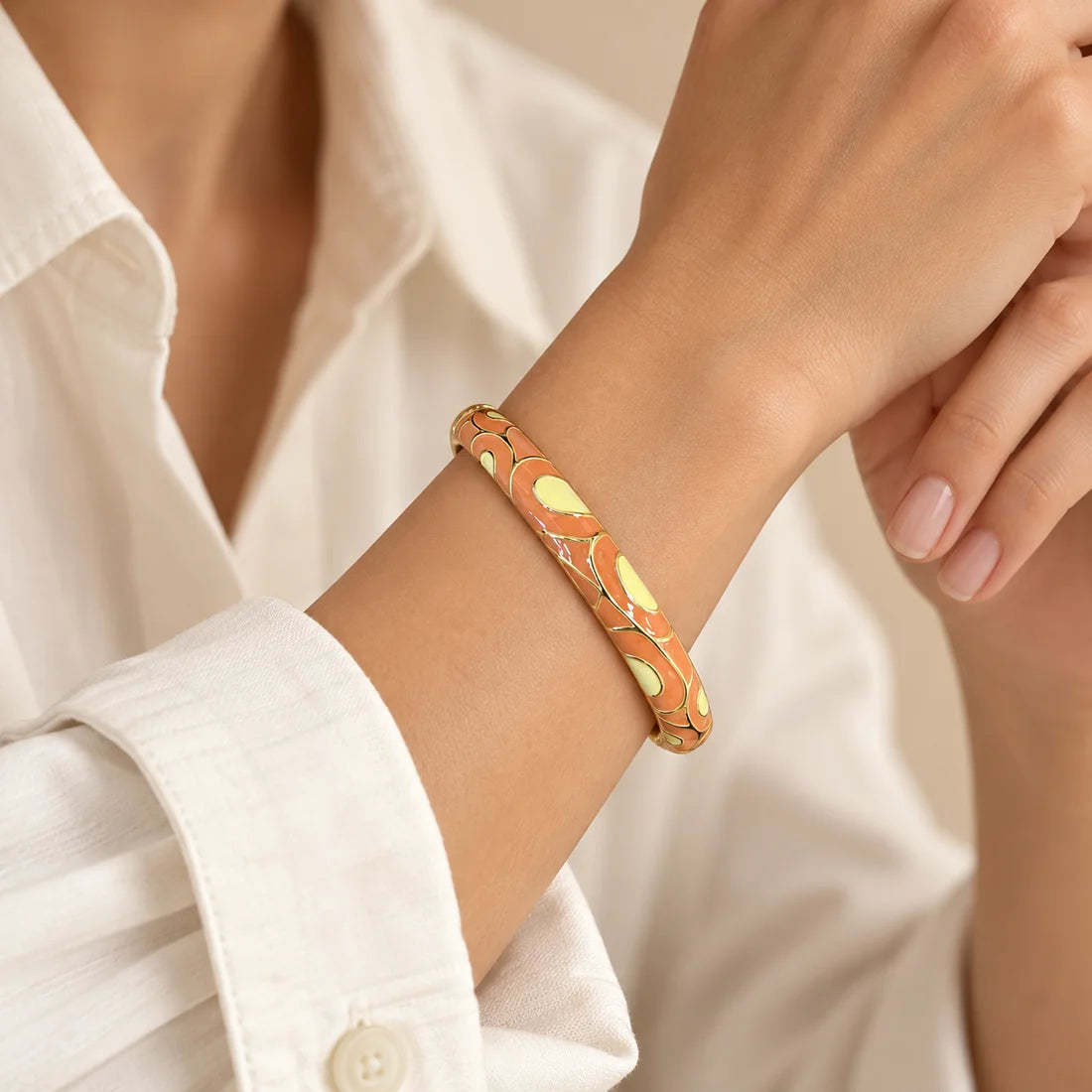 Apricot Swirl stainless steel bangle in peach, white with a swirl design, worn on a model wrist