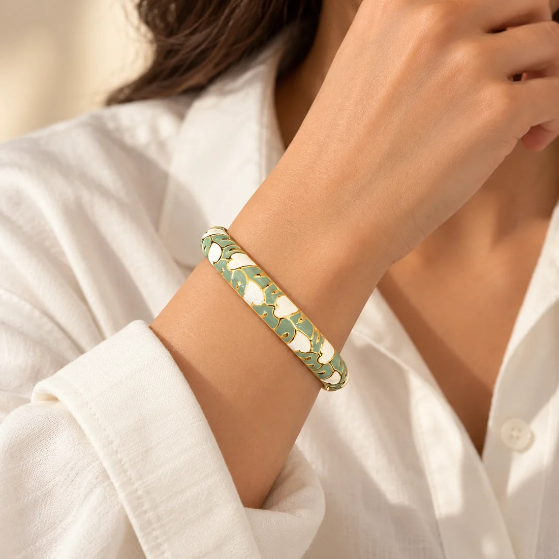 Sage Blossom stainless steel bangle in green, white with a floral design, worn on a model wrist