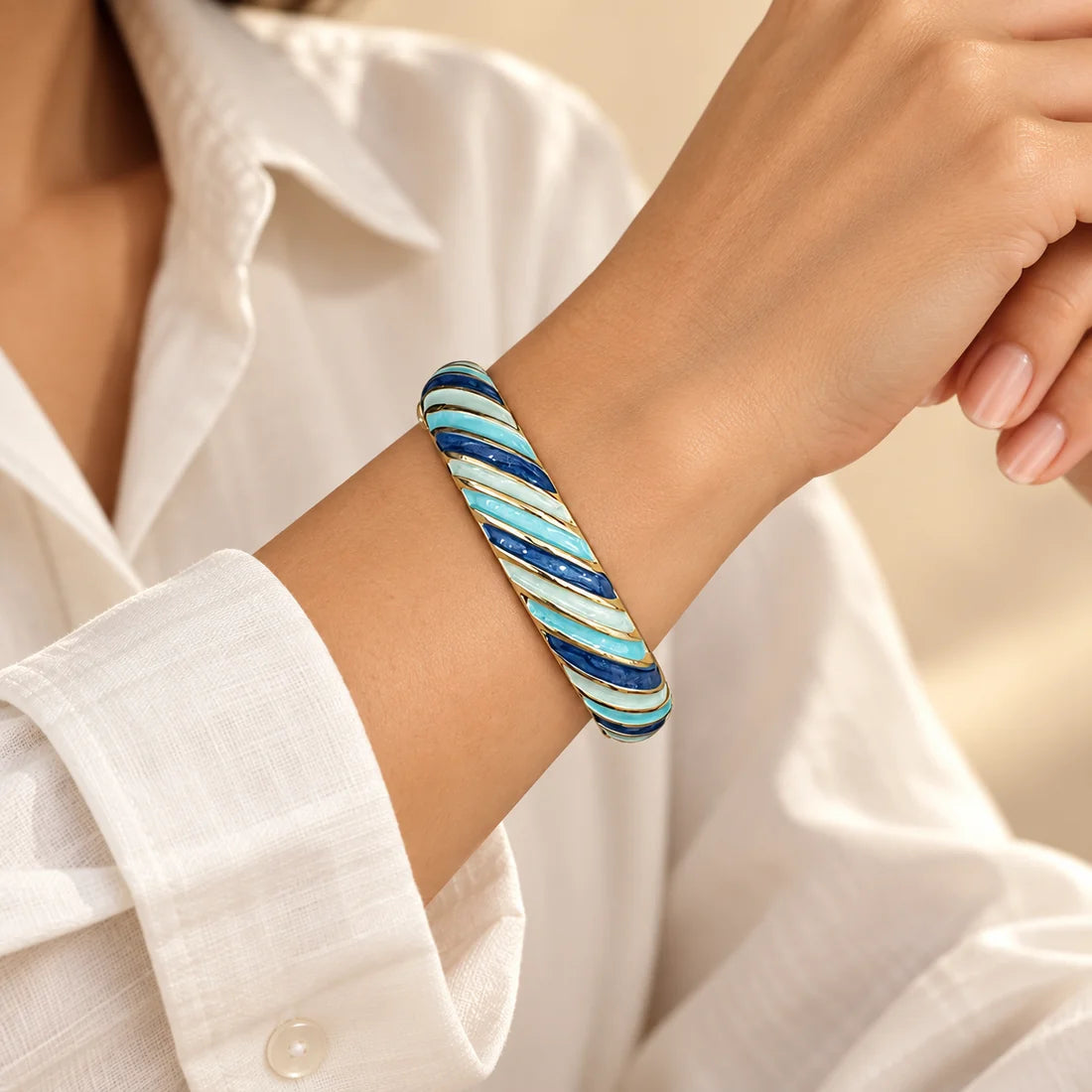 Ocean Ribbons stainless steel bangle in blue, white with a diagonal stripe design, worn on a model wrist