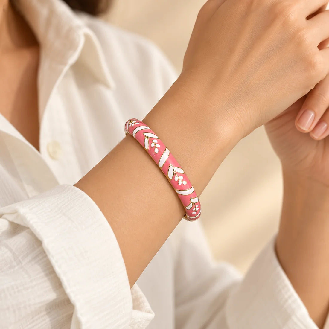 Rose Laurel stainless steel bangle in pink, white with a leaf design, worn on a model wrist