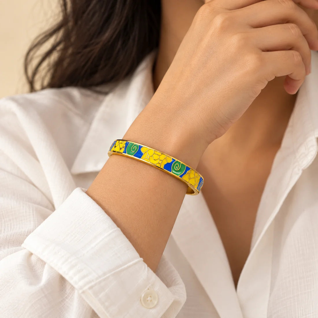 Sunlit Mosaic stainless steel bangle in yellow, blue with a geometric design, worn on a model wrist