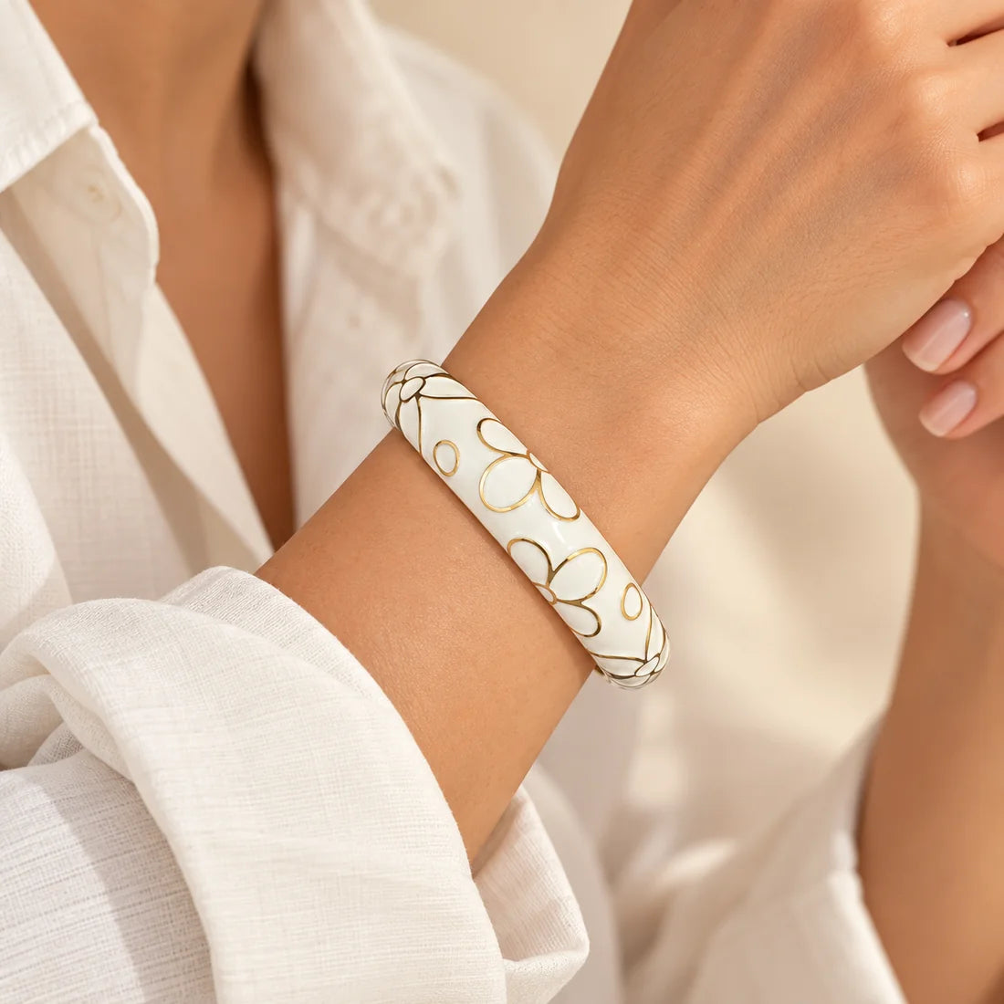 Ivory Blossom stainless steel bangle in white with a floral design, worn on a model wrist