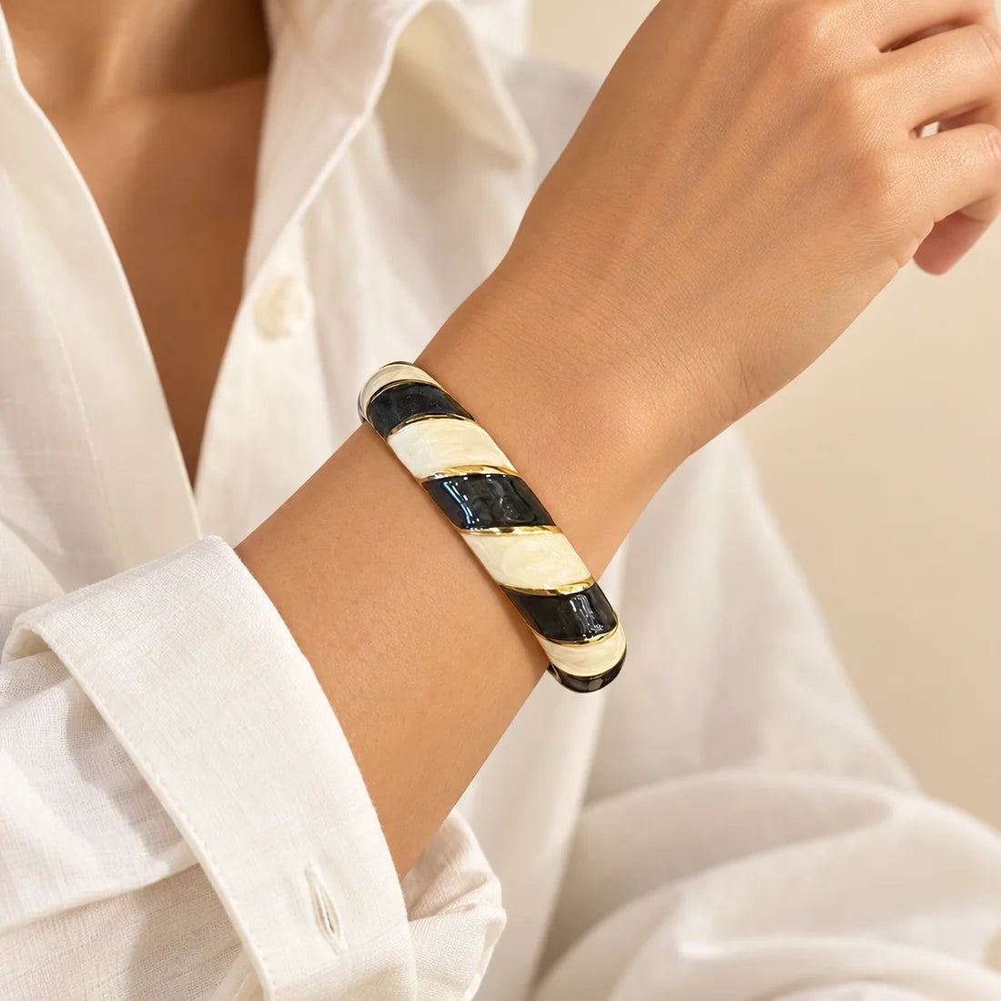 Noir Twist stainless steel bangle in black, white with a diagonal stripe design, worn on a model wrist