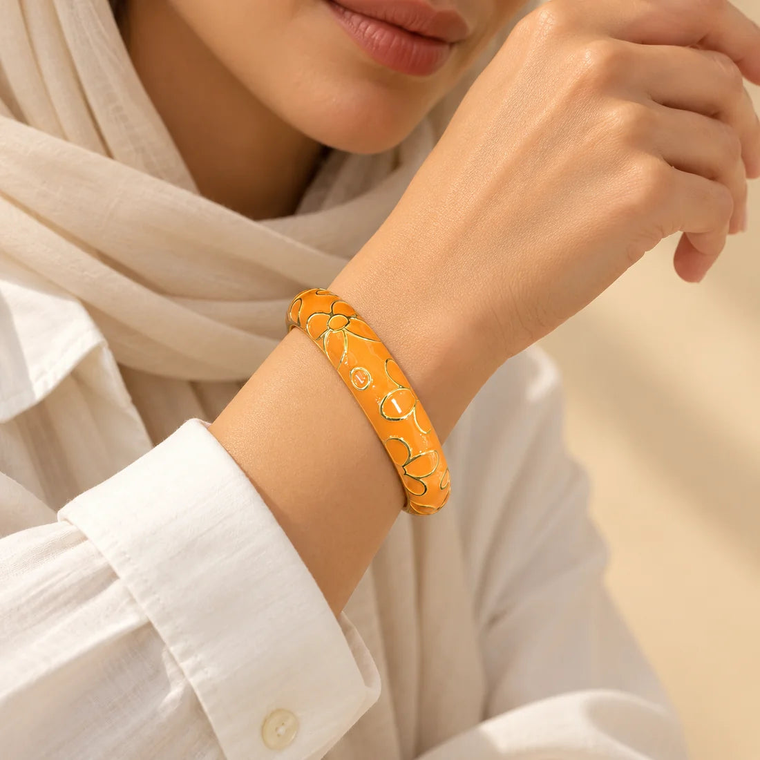 Tangerine Blossom stainless steel bangle in orange with a floral design, worn on a model wrist