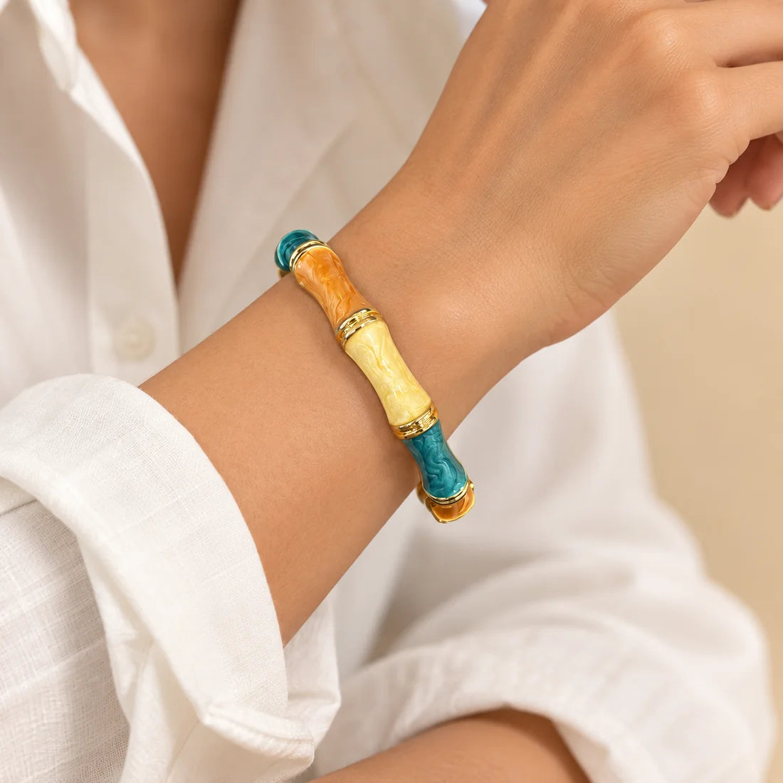 Amber Lagoon Bamboo stainless steel bangle in orange, yellow, turquoise with a colour block design, worn on a model wrist