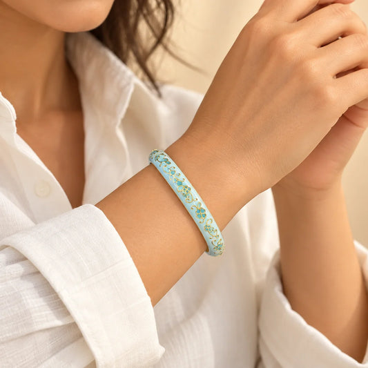 Sky Floral Lace stainless steel bangle in light blue, white with a floral design, worn on a model wrist
