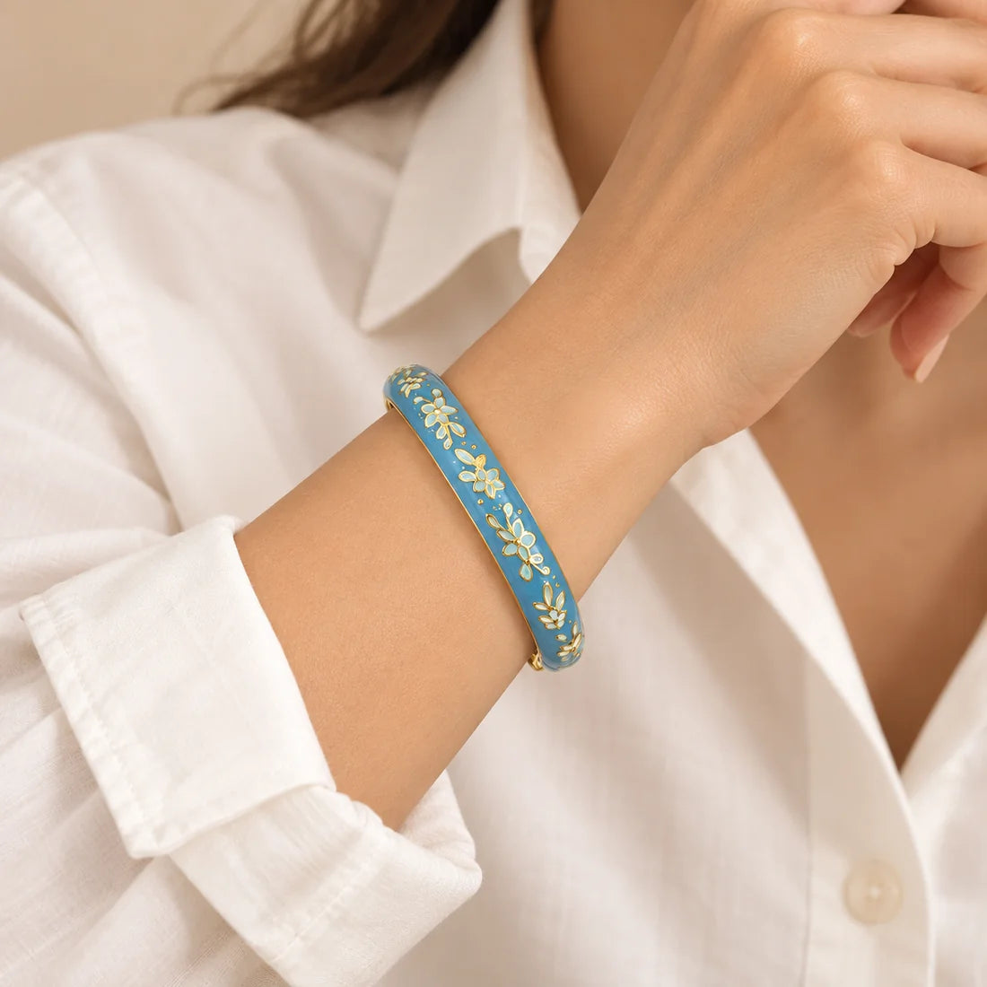 Blue Meadow stainless steel bangle in blue, white with a floral design, worn on a model wrist