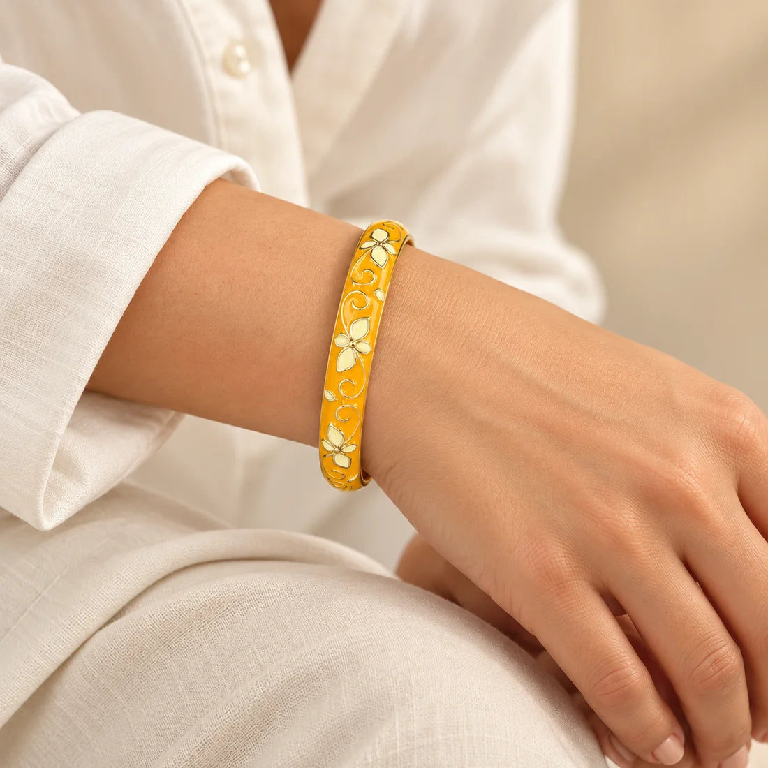 Marigold Scroll stainless steel bangle in yellow, white with a floral scroll design, worn on a model wrist