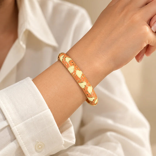 Apricot Petals stainless steel bangle in peach, white with a floral design, worn on a model wrist