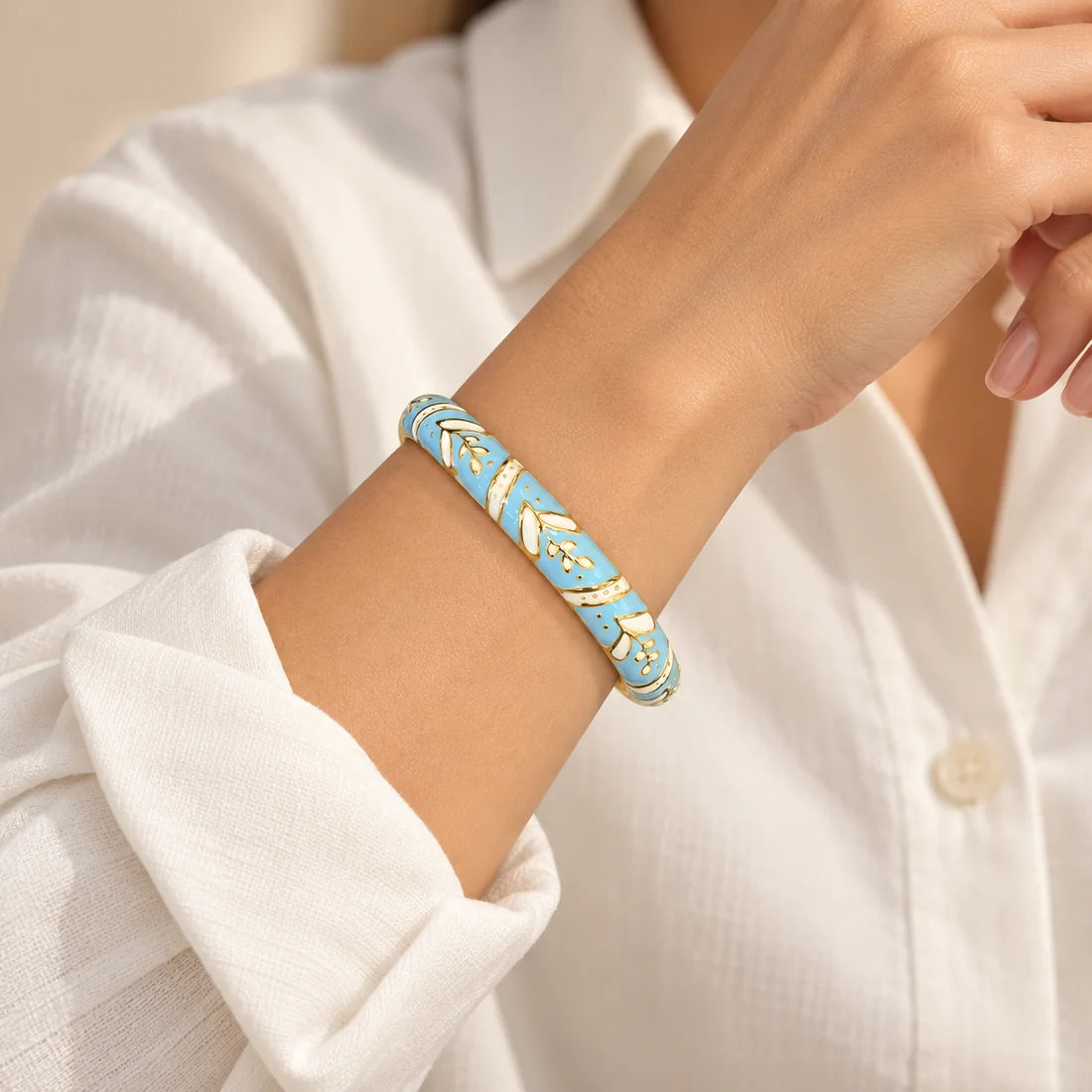 Sky Laurel stainless steel bangle in light blue, white with a leaf design, worn on a model wrist
