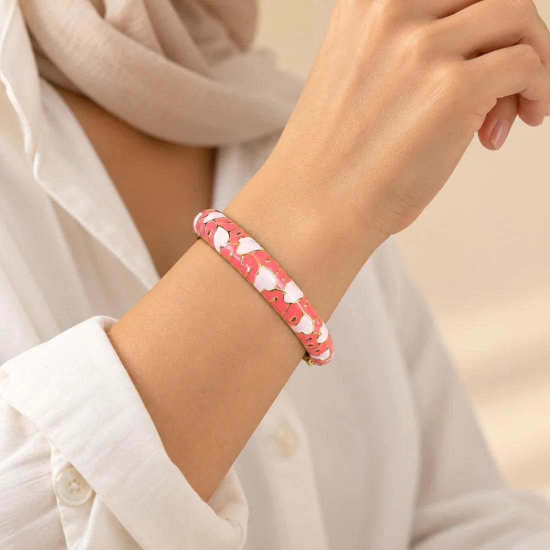 Coral Petals stainless steel bangle in coral, white with a floral design, worn on a model wrist
